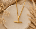 Gold T-bar pendant necklace on a fine curb chain, styled on a stone disc with pampas grass
