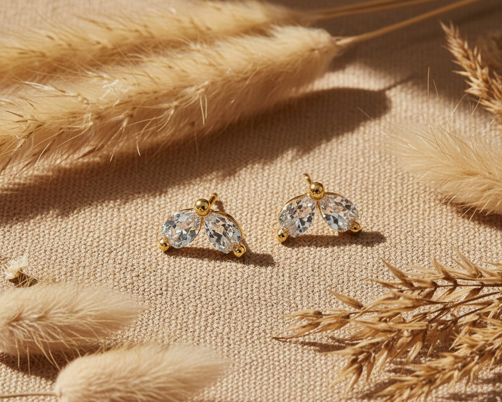 Gold crystal leaf stud earrings on boho linen background