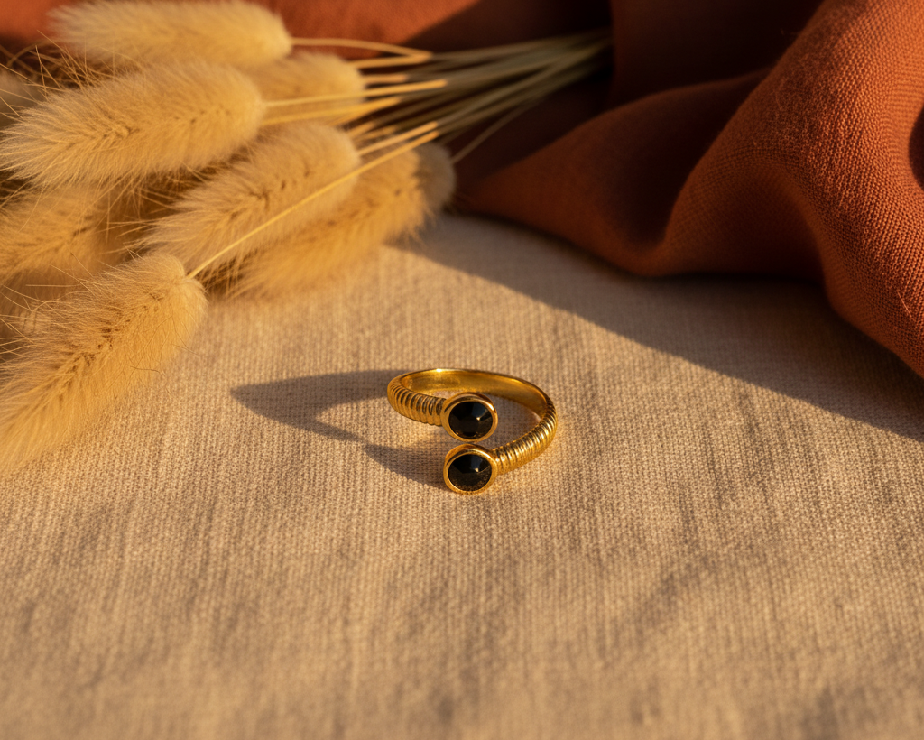 Gold ribbed open ring with black oval stones on boho background with pampas grass and terracotta fabric